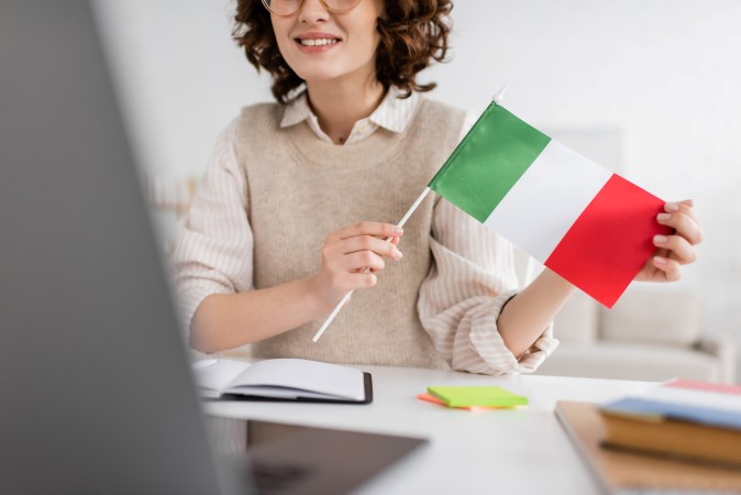 Θεματική εικόνα για το γιατί να μάθω ιταλικά. Καθηγήτρια κρατά στα χέρια της μια μικρή σημαία της Ιταλίας.