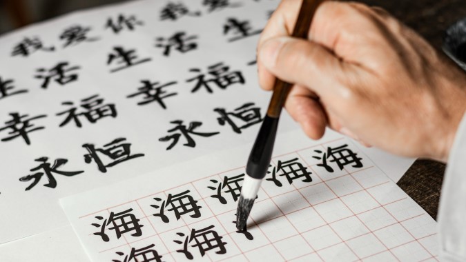 Θεματική εικόνα για το αν είναι δύσκολα τα κινεζικά. Μαθητής σχεδιάζει με πινέλο κινεζικούς χαρακτήρες.