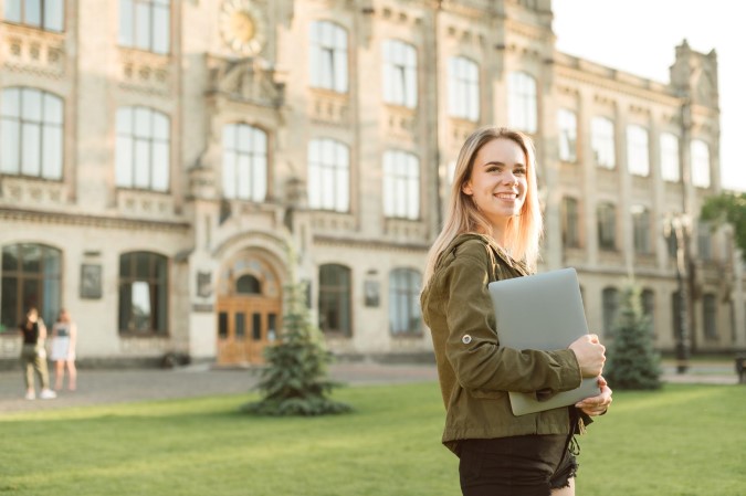 Θεματική εικόνα για προϋποθέσεις για μεταπτυχιακό στο εξωτερικό. Χαμογελαστή φοιτήτρια βρίσκεται μέσα σε πανεπιστημιακό campus.